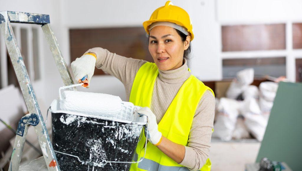 woman painter in a protective helmet and vest with paint roller