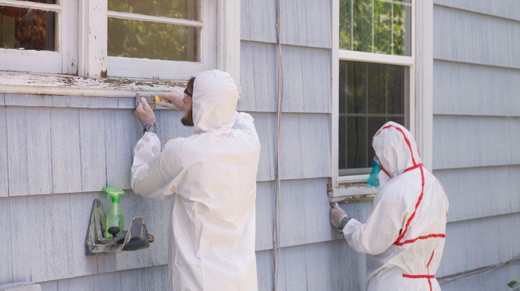 Two house painters in hazmat suits removing lead paint from an old house