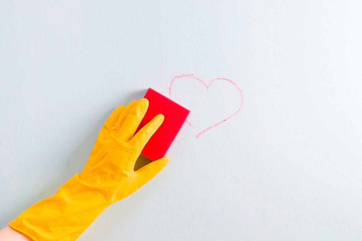 hand in a rubber yellow glove wipes a chalked heart on a wall with a sponge