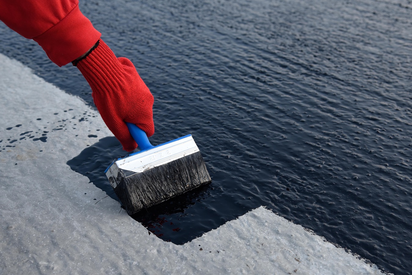 worker applies bitumen mastic on foundation