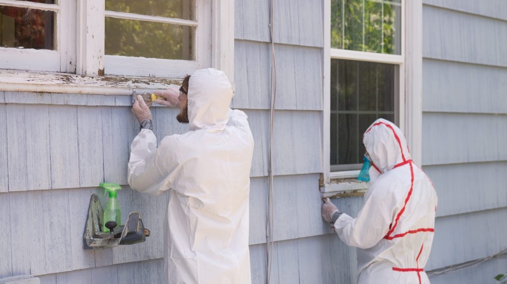 Two house painters in hazmat suits removing lead paint from an old house