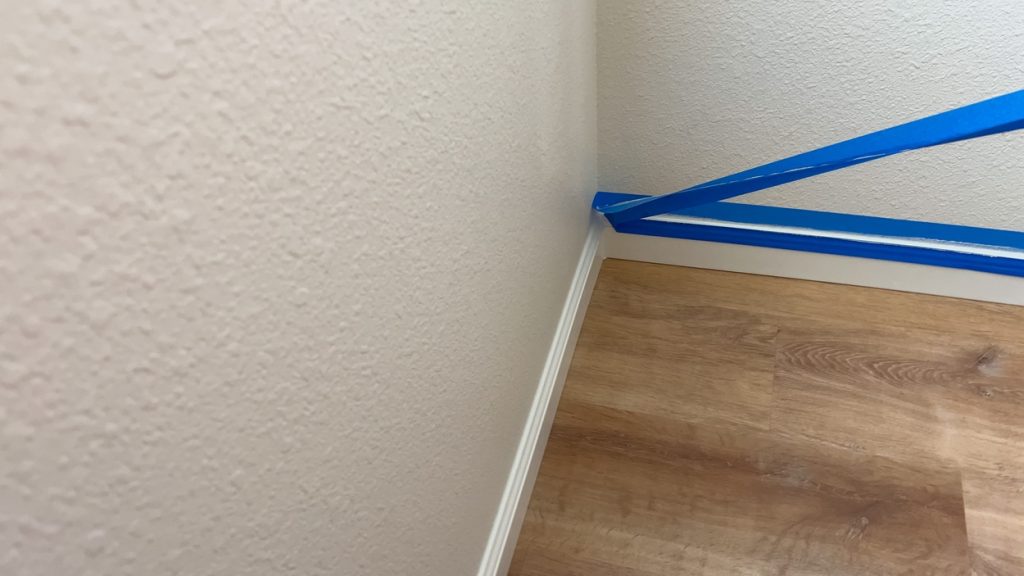 a corner section of a room with painters tape applied along the baseboard and adjacent walls