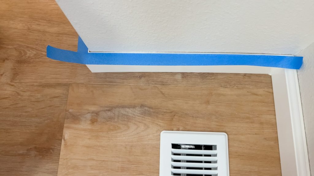 blue painter tape is neatly applied along baseboards and a corner wall junction above a wood floor