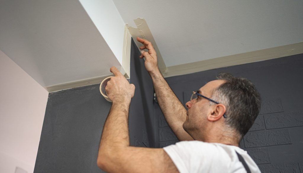 man sticks protective tape on the wall before painting