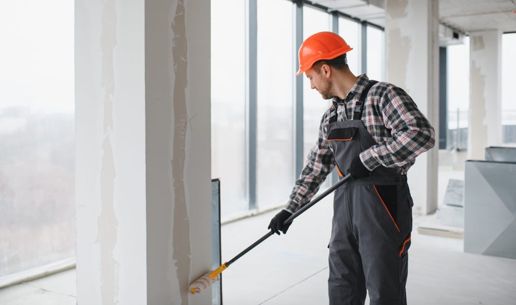 professional builder using a paint roller applying a fresh coat of paint to the walls of a building
