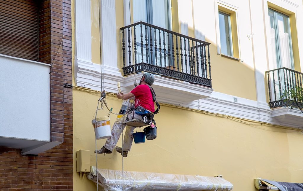worker paints building wall renovating works